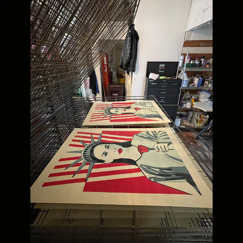 Art prints of a stylized face with red and white rays drying on a rack.