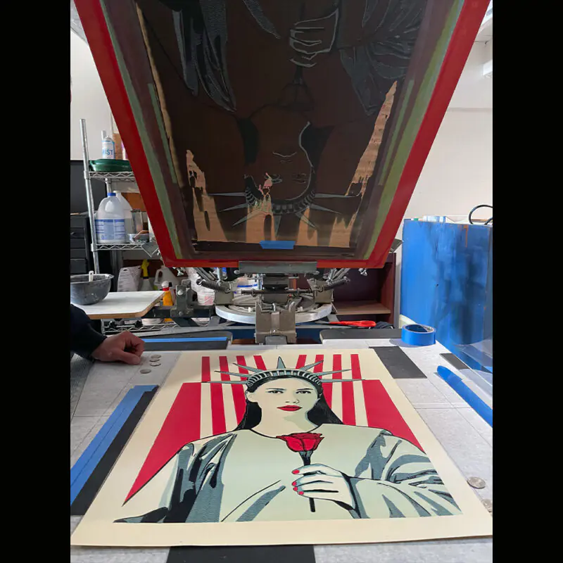 Artist painting a large, stylized patriotic portrait inside a workshop.
